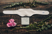 A beige neck and thyroid organic castor oil pack laid out flat with a piece of flannel, surrounded by decorative flowers and greenery.