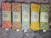 Set of five castor oil packs with floral patterns and visible branding on a gray surface.