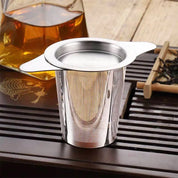 Stainless steel tea infuser on a wooden tea tray with a teapot in the background.