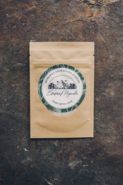 Paper tea package with a green and white label from Emma Magnolia on a dark stone surface