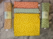 Five folded castor oil packs in yellow, green, and brown on a textured surface.