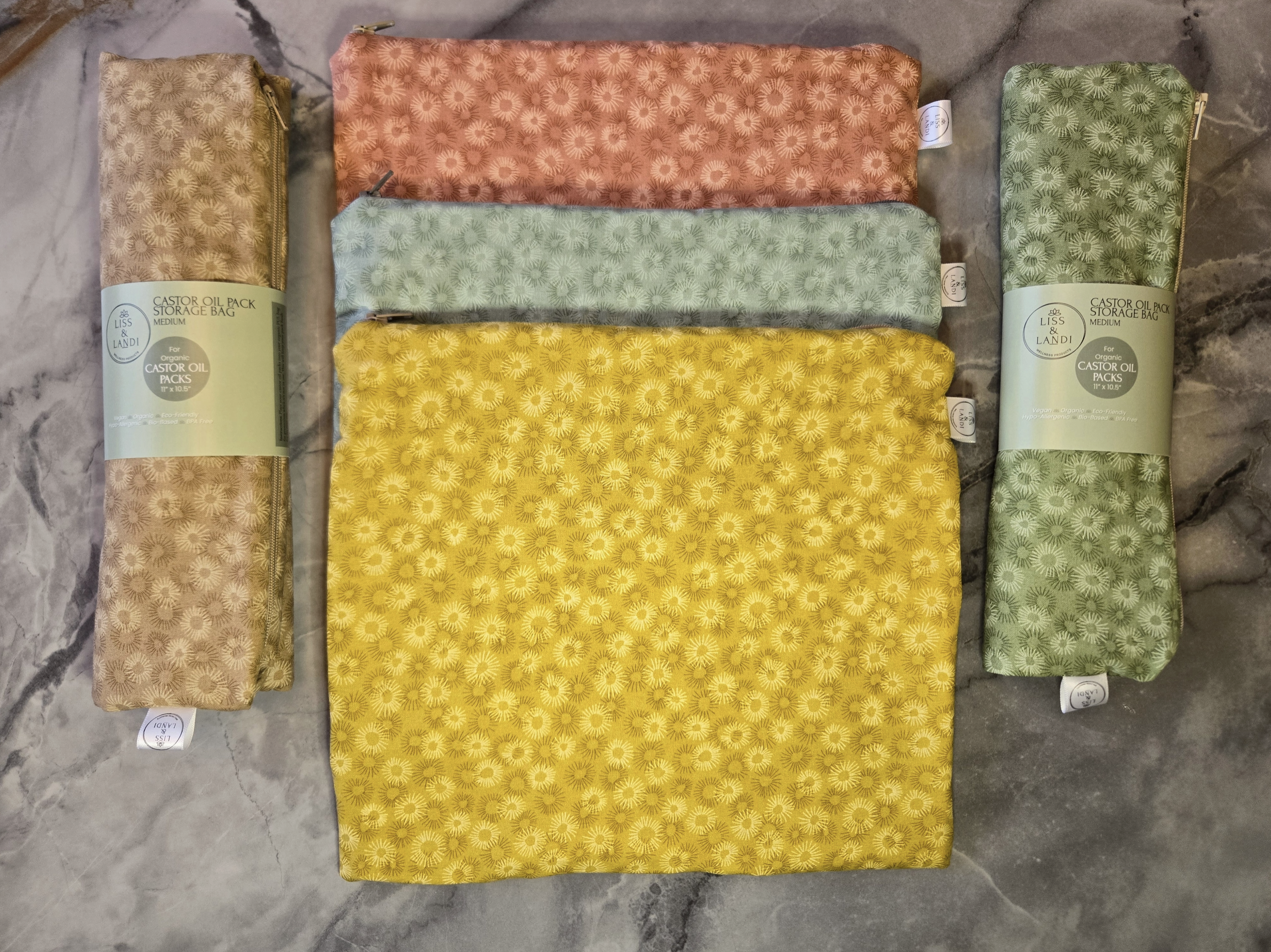 Five folded castor oil packs in yellow, green, and brown on a textured surface.