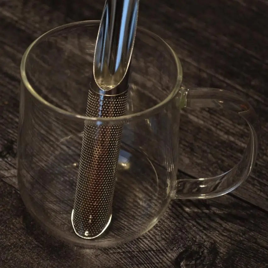 Metal tea infuser in a clear glass mug on a wooden surface