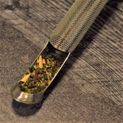 Metallic tea scoop and infuser filled with loose leaf tea on a textured surface