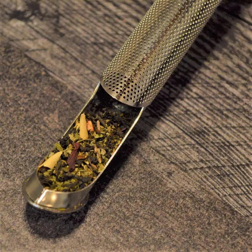 Metallic tea scoop and infuser filled with loose leaf tea on a textured surface